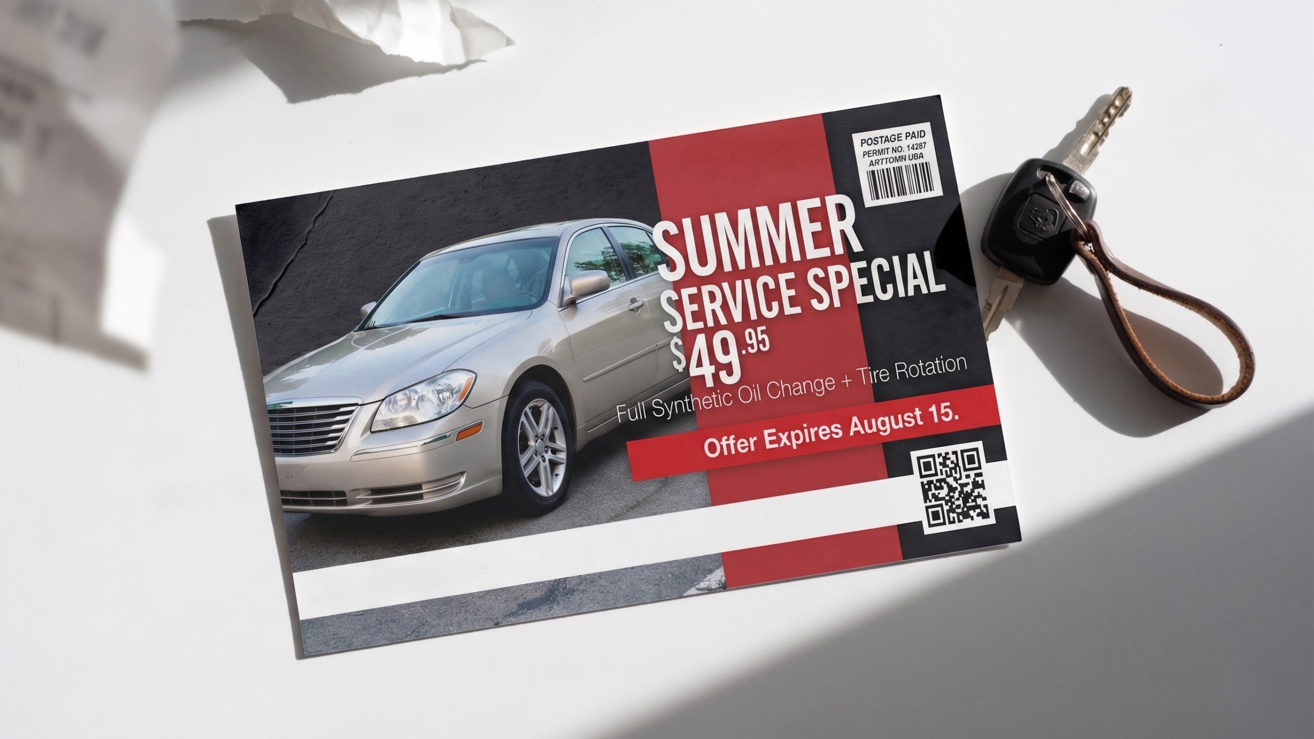 Photorealistic flat-lay of a printed 6×9 direct mail postcard lying on a light gray concrete surface. The postcard is landscape orientation and looks like it came off a commercial press — slight ink richness, real paper stock with a soft gloss finish, very subtle corner wear from handling. The postcard design: dark charcoal background, a bold full-bleed image of a silver sedan shot from a low three-quarter angle on the left half, occupying about 45% of the card. On the right half, a thick red vertical band anchors a white headline in heavy sans-serif type reading "SUMMER SERVICE SPECIAL" in two lines. Below it, a large white price callout: "$49" with ".95" in smaller superscript. Below the price, smaller body copy in light gray reads "Full Synthetic Oil Change + Tire Rotation" and below that a bold red deadline bar with white text: "Offer Expires August 15." Bottom strip of the card: a white bar with a phone number, a QR code placeholder square, and a small USPS indicia box in the far right corner. The postcard looks real and used — not a mockup, not a template screenshot, not a 3D render. Photographed from directly above with soft diffused daylight. No people. No company name or logo anywhere on the card.